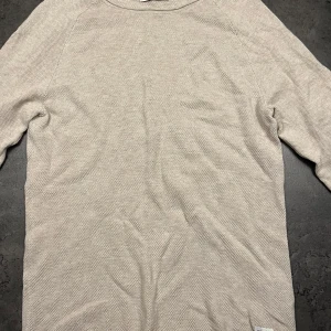 Beige långärmad stickad tröja från Jack & Jones - Säljer en stilren beige långärmad stickad tröja från Jack & Jones. Perfekt för både vardag och lite finare tillfällen. Tröjan är i ett mjukt material och har en klassisk passform. Den är i mycket bra skick och redo för en ny ägare! Nypris 450:-