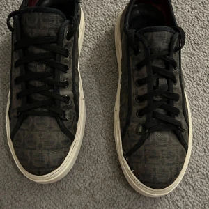 Salvatore Ferregamo skor - Ferragamo sneakers Svarta/gråa med vit sula storlek 44. De är lite slitna (se bild 3) men inget som syns när man har på sig dem.   Tags: Fendi Louis Vuitton guizeppe zanotti dondup grisch Armani Gucci Lv Chanel burberry Lacoste Louboutin 