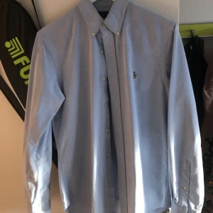 Blå skjorta från Ralph Lauren - Säljer en snygg blå skjorta från Ralph Lauren i slim fit. Skjortan har långa ärmar och klassiska knappar framtill. Den är i bomull och har den ikoniska broderade loggan på bröstet. Perfekt för både vardag och fest! 💙