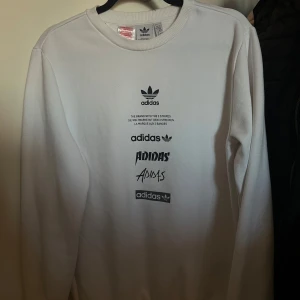 Vit långärmad tröja från Adidas - Säljer en stilren vit långärmad tröja från Adidas med flera olika logotyper tryckta på framsidan. Passar S/M 176 i barn storlek 