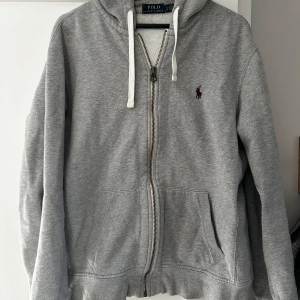 Ralph lauren zip hoodie grå - Snygg zip hoodie från Ralph lauren. Tröjan är i väldigt bra skick. Den är i storlek L men skulle säga att den passar perfekt för storlek M