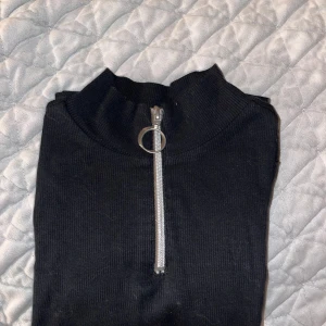 Svart ribbad tröja med dragkedja - Säljer en svart ribbad tröja med en dragkedja framtill. Den har långa ärmar och en liten ståkrage. Perfekt för höst och vinter, och funkar både till vardags och fest. Tröjan är i bra skick och superbekväm att ha på sig.