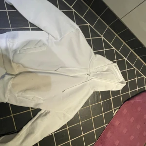 Vit hoodie med dragkedja - Säljer en vit hoodie med dragkedja. Den är perfekt för en avslappnad stil och har en klassisk passform. Hoodien har fickor framtill och en bekväm huva. Perfekt för kyliga dagar eller som ett lager under jackan.
