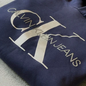 Mörkblå hoodie från Calvin Klein - Säljer en snygg mörkblå hoodie från Calvin Klein. Den har en logga på framsidan och har en skön och snygg luva. I övrigt är tröjan i väldigt fint skick // hör av dig vid funderingar 