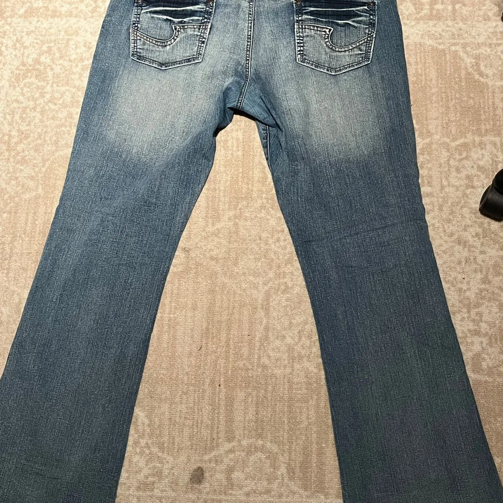 Säljer ett par snygga blå jeans i bootcut-stil. De har en klassisk femficksdesign med knappar och dragkedja fram. Jeansen har en lätt slitning för en cool, avslappnad look. Perfekta för både vardag och fest!. Jeans & Byxor.