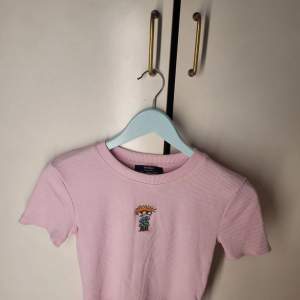 Säljer en söt rosa ribbad t-shirt från Bershka med ett litet Rugrats-motiv på bröstet. Perfekt för en avslappnad stil. T-shirten är i mycket bra skick och har korta ärmar. Passar perfekt till vår och sommar!