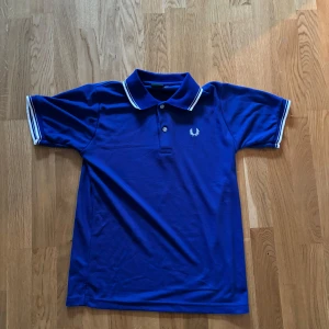 Blå pikétröja från Fred Perry - Säljer en s blå pikétröja från Fred Perry i storlek S. Tröjan har vita detaljer på kragen och ärmsluten samt den klassiska Fred Perry-loggan broderad på bröstet. 