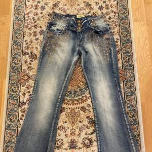 Snygga blå jeans med låg midja och bootcut-stil köpta i en secondhandbutik. De har coola paljettdetaljer och knappar framtill. Perfekta för en festlig look! 🕺✨Jag har sytt om midjan så att de skulle passa mig mer för jag är så petit, men har aldrig kommit till användning av mig. Originella storleken var 30 men skulle nog säga att de är ungefär storlek 27 nu och sitter lite baggy på benen. Midjemåttet tvärs över är 37cm 💕💕