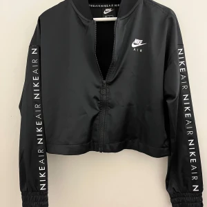 Svart bomberjacka från Nike - Säljer en snygg svart bomberjacka från Nike Air. Jackan har en dragkedja framtill och långa ärmar med texten 'NIKE AIR' längs sidorna. Perfekt för en sportig look eller casual vardagsstil. Passar bra till både höst och vår!😎🖤💘