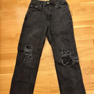 Svarta jeans med slitningar från NA-KD - Säljer ett par svarta jeans från NA-KD i bra skick. De har coola slitningar på knäna som ger en edgy look. Perfekta för en avslappnad stil. Jeansen har en klassisk femficksdesign och knappgylf. Passar perfekt till både vardag och fest!🖤💘