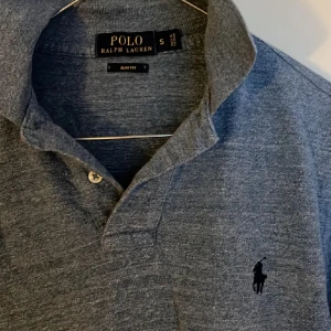 Gråblå pikétröja från Ralph Lauren - Säljer en stilren gråblå pikétröja från Ralph Lauren i storlek S. Tröjan är i slim fit och har den klassiska broderade loggan på bröstet. Köpt i Italien