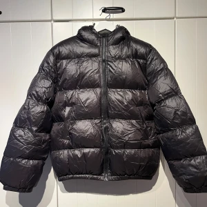 Svart glansig pufferjacka - Säljer en svart pufferjacka i mycket bra skick. Köpt second hand utan lappar.