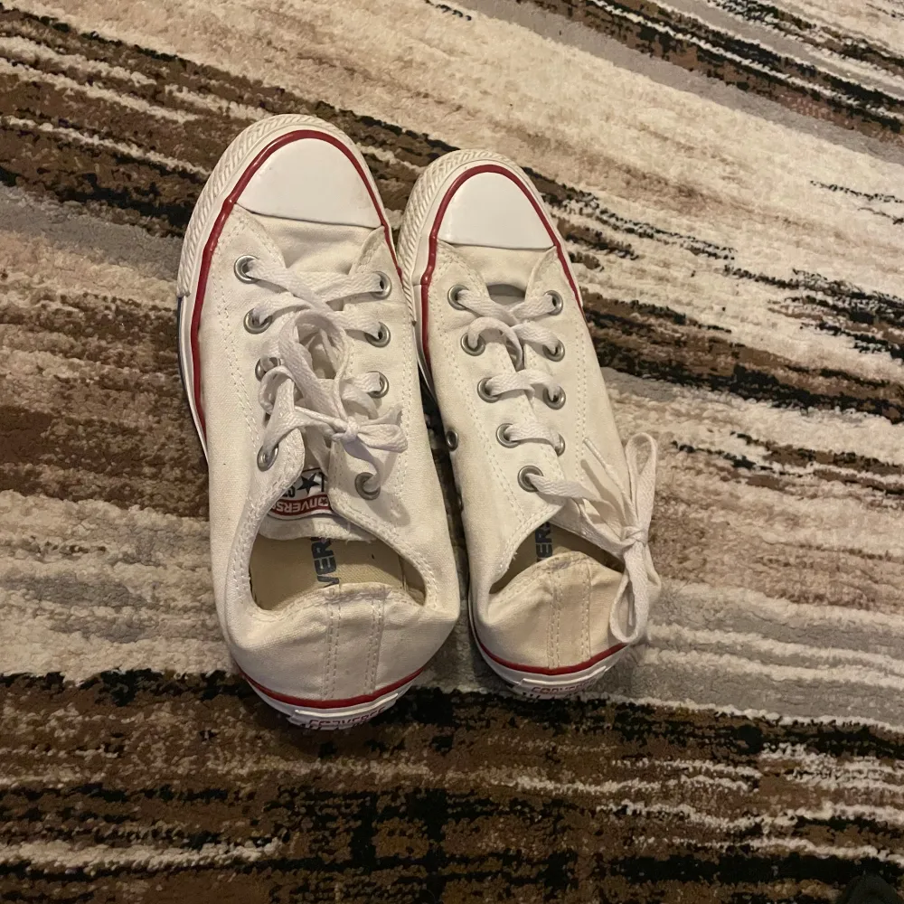 Säljer ett par klassiska vita Converse sneakers i bra skick. De har den ikoniska röda och blå randen runt sulan och är perfekta för vardagsbruk. Skorna har snörning och är i storlek herr 42. Passar perfekt till både jeans och shorts!. Skor.