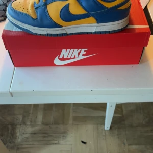 Nike Dunk Low Retro - Säljer ett par Nike Dunk Low Retro i blått och gult. Skorna är i mycket bra skick och kommer i originalkartong. Perfekta för både vardag och festliga tillfällen. Storlek och passform är normal.