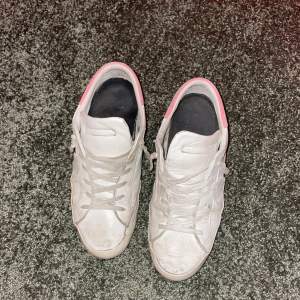 Säljer ett par vita sneakers med rosa detaljer och röd sula. De har snörning och är i bra skick, men lite smutsiga. Perfekta för vardagsbruk och ger en cool touch till din outfit. Pris kan diskuteras