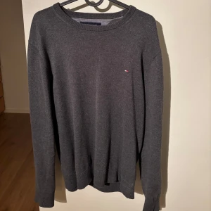 Grå tröja från Tommy Hilfiger - Säljer en stilren grå tröja från Tommy Hilfiger i storlek M. Tröjan är tillverkad i en mjuk blandning av pima bomull och kashmir, vilket gör den superbekväm. . Perfekt för både höst och vinter!