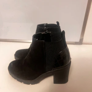 Svarta boots med klack - Snygga svarta boots i mocka med klack och dragkedja på sidan. De har en stilren design med elastiska paneler för bättre passform. Perfekta för höst och vinter, både till vardags och fest.