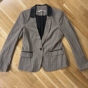 Kavaj - Säljer en snygg rutig kavaj från Truly by part two i storlek 38 EUR. Den har en klassisk design med svarta detaljer på kragen och fickorna. Kavajen har långa ärmar och en knapp framtill.