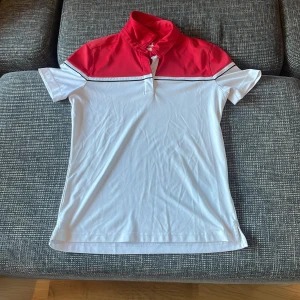 Vit och röd pikétröja från Cutter & Buck - Säljer en snygg vit och röd pikétröja från Cutter & Buck i storlek M. Tröjan har en klassisk krage och korta ärmar, perfekt för golf eller andra utomhusaktiviteter. Den är i mycket bra skick och har en stilren design med en diskret logga på baksidan. Pris går alltid att förhandlas!