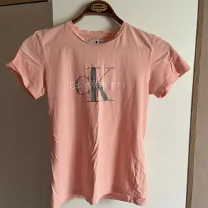 Säljer en snygg rosa t-shirt från Calvin Klein Jeans. Den är kortärmad och har en stilren logga på framsidan. Perfekt för en avslappnad look eller att styla upp med accessoarer. Passar bra till både jeans och kjol. Skön och bekväm att ha på sig hela dagen!