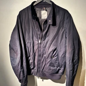 Marinblå bomberjacka från J.Lindeberg - Snygg marinblå bomberjacka från J.Lindeberg i bra skick. Den har en dragkedja framtill och praktiska fickor med knappar. Perfekt för höst och vår, med en stilren look som funkar till det mesta. Jackan är långärmad och har en klassisk passform. Jackan har lite ”rivmärken” på ryggen men de syns knappt. Köpt för 3000kr på NK. Tveka inte att höra av dig om du har frågor eller vill ha fler bilder 