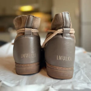 Inuikii-boots strl 38 - Säljer ett par beiga inuikii. Väl omhändertagna, men har inte använts på länge utan legat i en flyttkartong sista tiden. Ett av fästena som håller fast banden har släppt på ena skon. Storlek 38. Nypris ligger kring 3000 kr. 