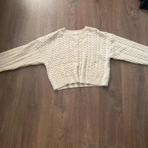Beige stickad tröja från Lindex - Säljer en superfin beige stickad tröja från Lindex i storlek 146/152. Den har ett snyggt flätmönster på ärmarna och är croppad för en modern look. Perfekt för höst och vinter! 🧶