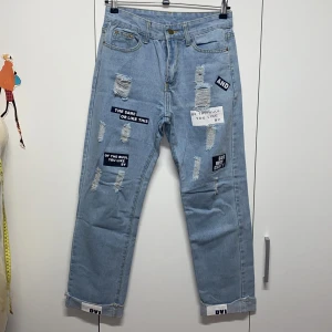 Ljusa jeans med tryck och slitningar - Säljer ett par ljusa jeans med coola tryck och slitningar. De har en loose passform och är perfekta för en avslappnad stil. Jeansen har uppvikta benslut och flera tryck med text på framsidan. Perfekta för både vardag och fest!