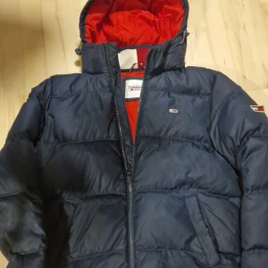 Tommy Hilfiger puffer dunjacka - Säljer en snygg navy blå dunjacka från Tommy Hilfiger. Den har en röd insida. Tjock och extremt varm och vindtät. I gott skick. Storlek L men uppfattas som mindre. Några små repor på en arm. Modellen på bilden är 182 cm, väger 72 kg.