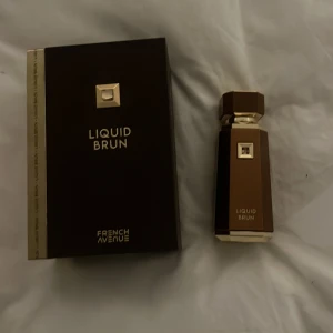Liquid Brun parfym från French Avenue - Säljer en elegant parfymflaska från French Avenue, Liquid Brun. Flaskan är brun och guld med en fyrkantig form och en stilren design. Perfekt för den som gillar en lyxig och sofistikerad doft. Kommer i originalförpackning.