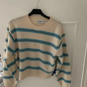 Randig tröja från Weekday - Säljer en superfin randig tröja från Weekday i beige med blå och turkosa ränder. Den är i bra skick och perfekt för både vår och höst. Tröjan har en normal passform och långa ärmar, vilket gör den mysig och stilren. Perfekt för en casual look!