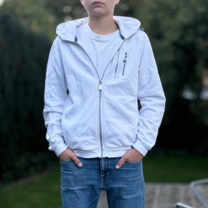 Sail racing zip hoodie vit barn - Säljer en vit huvtröja från Sail racing i bomull. Den har en dragkedja framtill och långa ärmar. Tröjan är i bra skick men har ett litet hål och slitage vid ärmslutet. Perfekt för vardagsbruk och under en jacka på vintern. Dragkedjan på bröstat är lite trasig men funkar fortfarande, modellen är 160. Vid intresse för fler bilder eller frågor hör gärna av dig☺️
