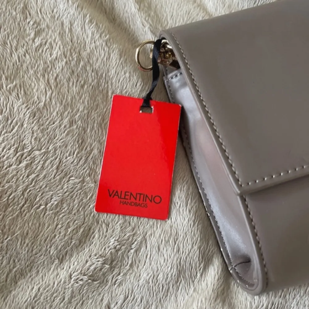 Snygg beige axelväska från Valentino i mycket bra skick. Väskan har en elegant kedjerem och en dekorativ tofsdetalj framtill. Perfekt för både vardag och fest! 👜✨. Laukut & Käsilaukut.