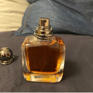 Stronger With You Intensely från Emporio Armani - Säljer en elegant parfymflaska av Stronger With You Intensely från Emporio Armani. Flaskan är i glas med en varm bärnstensfärgad vätska och har en stilren, rundad design. Perfekt för den som vill ha en intensiv och sofistikerad doft. Korken är metallisk och ger en lyxig känsla.
