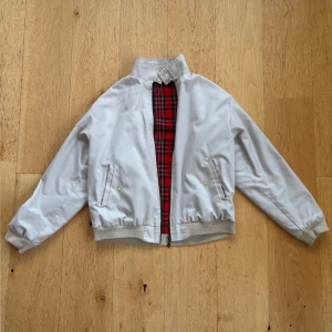 Beige Harringtonjacka från Merc - Säljer en klassisk beige Harringtonjacka från Merc. Den har ett snyggt rött rutigt foder och ribbade muddar. Perfekt för höst och vår! Jackan har en dragkedja framtill och två fickor med knappar. Made in England, så den har riktigt bra kvalitet. Passar både till vardags och lite finare tillfällen.