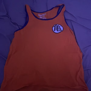 Orange Dragon Ball Z linne - Säljer ett coolt orange linne med Dragon Ball Z-tema från Ripple Junction. Linnet har svarta kanter och två tryck med japanska tecken på fram- och baksidan. Perfekt för fans av serien! Tillverkat i 100% bomull.