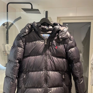 Ralph Lauren Jacka, svart/glansig - Dags för mig att Sälja min super trendiga Ralph Lauren jacka, den är i storlek L och oerhört fint skick (10/10). Köpt förra vintern och endast använd vid fåtal tillfällen. Ny pris 6 095kr! Kom med bud och tveka inte med att ställa frågor! Mvh Oscar 