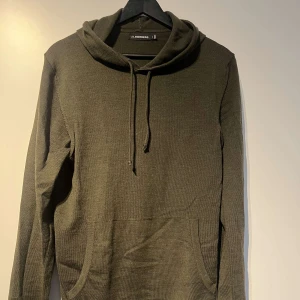 Merinoull hoodie J.Lindeberg - Säljer en snygg och bekväm mörkgrön hoodie från J.Lindeberg. Perfekt för höst och vinter med sin mjuka och varma känsla. Den har en klassisk känguruficka och justerbar huva med dragsko. Passar perfekt för en avslappnad stil!