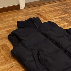 Dunväst från ESPRIT - Säljer en svart dunväst från ESPRIT i mycket bra skick. Västen har en dragkedja framtill och är perfekt för höst och vinter. Den är tjock och är riktigt varm och skön ut. Perfekt för lager-på-lager-stil när det är kyligt ute. Det finns även en luva som går att ta fram där bak. Endast: 299