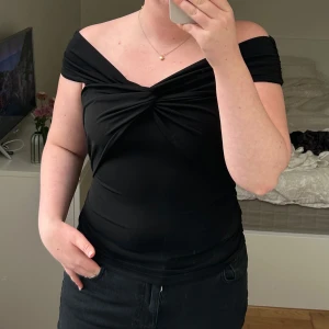 Svart offshoulder topp - Snygg svart offshoulder topp med en knutdetalj framtill. Toppen har en tight passform och är gjord i ett mjukt och stretchigt material som sitter bekvämt. Storlek L, passar M