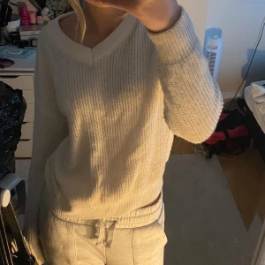 Vit stickad tröja - Mysig vit stickad tröja med v-ringning och långa ärmar. Perfekt för kyliga dagar och passar till både jeans och mjukisbyxor. Tröjan har en avslappnad passform och ribbade muddar vid ärmslut och nederkant.