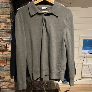 Grå tröja från Filippa K - Säljer en stilren grå tröja från Filippa K i storlek S. Tröjan är tillverkad av en mjuk blandning av bomull och ull, perfekt för både höst och vår. Den har en klassisk krage och långa ärmar, vilket gör den både bekväm och snygg. Passar perfekt till uppklädda och soft outfits!