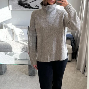 Grå stickad polotröja - Mysig grå stickad polotröja med hög krage, perfekt för kyliga dagar. Tröjan har en avslappnad passform och långa ärmar, vilket gör den idealisk för både höst och vinter. Den ribbade kanten ger en snygg detalj och extra komfort. Perfekt att mysa i hemma eller för en avslappnad dag ute.