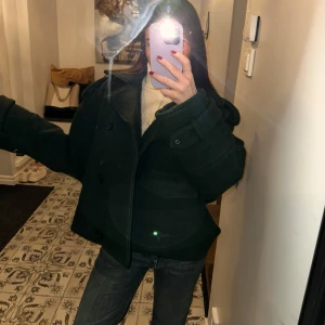 Mörkgrön kappa - Säljer en snygg unik mörkgrön kappa ifrån Alhvar Gallery i mycket bra skick. Den har en klassisk design med dubbelknäppning och stora knappar. Perfekt för höst och vinter, och den är långärmad för extra värme. Passar bra till både vardag och fest! 100% ull och viskos. Den är använd fåtal gånger & har mest bara hängt i garderoben och nu varit nerpackad på vinden i ca 1 år. Köptes för 2 vintrar sedan. Super varm och gosig. Jackan har en oversized passform så xs sitter som M 