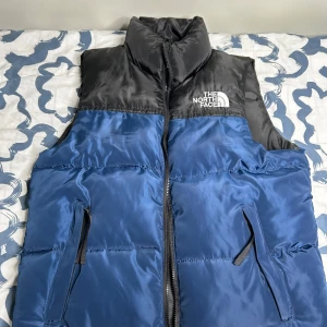 The North Face väst - Säljer en snygg blå och svart dunväst från The North Face i storlek M för att jag bytte stil. Västen är jätte varmt framtill och är perfekt för kyliga dagar. Den är i mycket bra skick och knappt använt. Pris kan bli diskuteras och skriv för mer info!