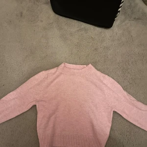 Rosa stickad tröja - Mysig rosa stickad tröja i mycket bra skick. Perfekt för kyliga dagar med sin varma och bekväma design. Tröjan har långa ärmar och ribbade kanter vid ärmslut och nederkant. Enkelt att matcha med jeans eller kjol för en avslappnad look. Jag skulle säga att den stämmer bra överens med storleken 