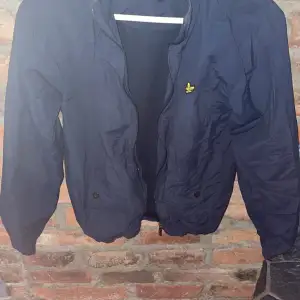 Säljer en snygg mörkblå bomberjacka från Lyle & Scott i juniorstorlek 14/15 år. Jackan har en dragkedja framtill och två knappar vid fickorna. Perfekt för höst och vår med sin stilrena design och bekväma passform. Den ikoniska gula loggan syns på bröstet. Passar både till vardags och lite finare tillfällen. Köpt för några år sen och andvänt flitigt därmed de låga priset 