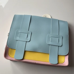 Flerfärgad barn ryggsäck - Superfin ryggsäck i pastellfärger! Den har en cool kombination av blått, rosa och gult. Väskan har en praktisk design med dubbla spännen. Perfekt för vår och sommar när du vill ha något färgglatt och stilrent. För barn 👜✨