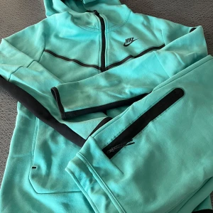 Nike tech fleece - Turkos hoodie och byxor  - Säljer en snygg turkos Nike tech fleece track suit från Nike i mycket bra skick. Den har en dragkedja framtill och svarta detaljer längs ärmarna och huvan. Perfekt för träning eller en chill dag. 