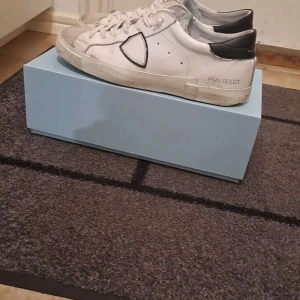 Philippe Model vita sneakers - Säljer ett par vita Philippe Model sneakers i bra skick. De har svarta detaljer och en klassisk design med snörning. Perfekta för vardagsbruk och stilrena till de flesta outfits. Tillverkade i Italien. Priset går att diskutera och de är i storlek 42 men passar större